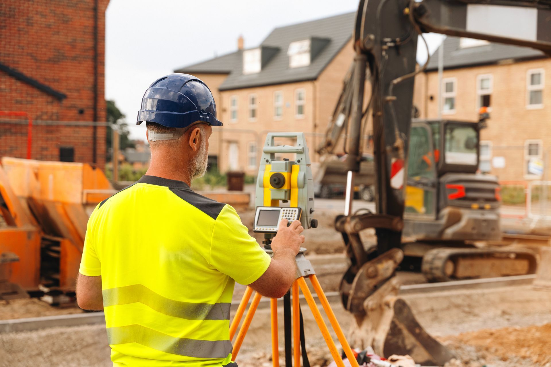 Surveyor using a total station on a construction site, wearing a safety vest and helmet.