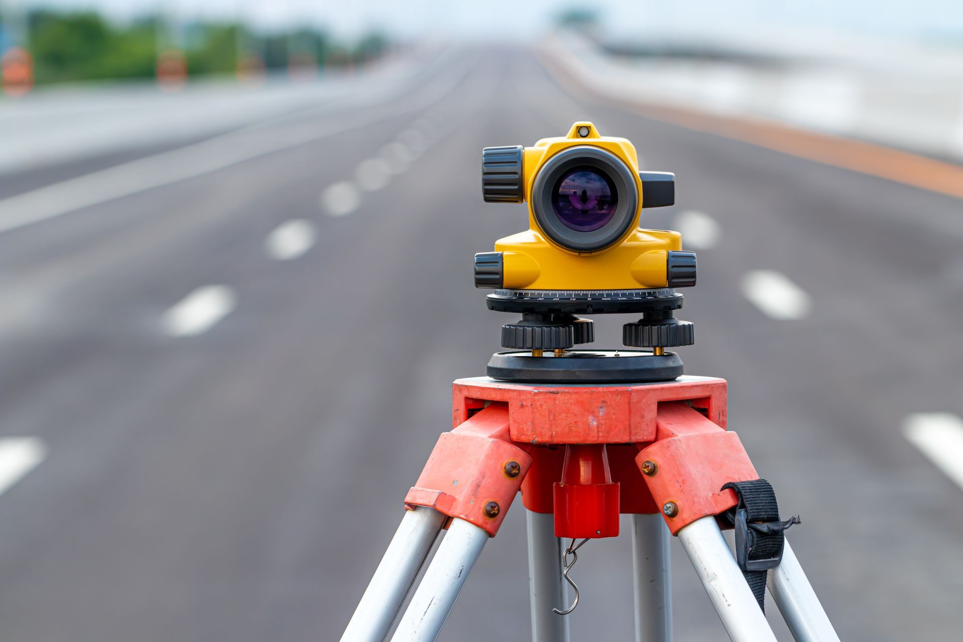 Yellow surveying instrument on a tripod, set up on a road, blurred background.