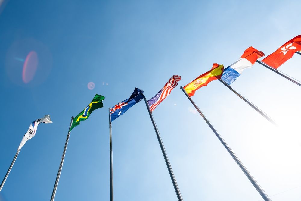 Flags of various nations waving in the bright blue sky.