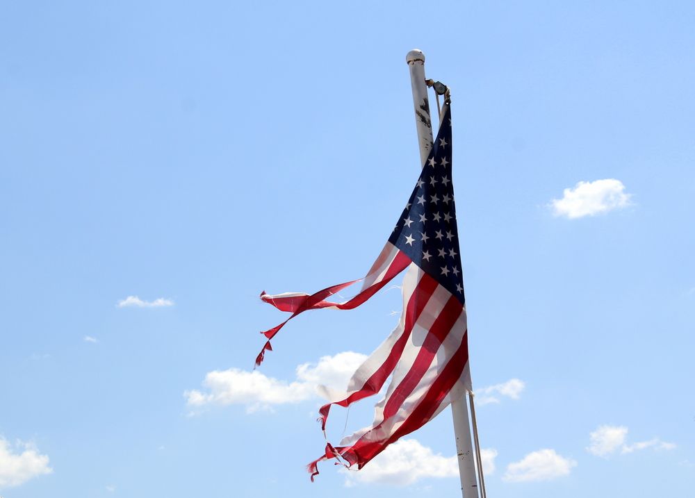 Tattered American flag on a pole against a partly cloudy, blue sky.