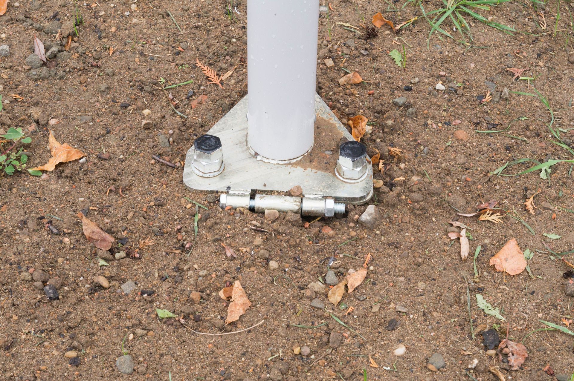 Gray metal pole bolted to a concrete base, set in green grass.