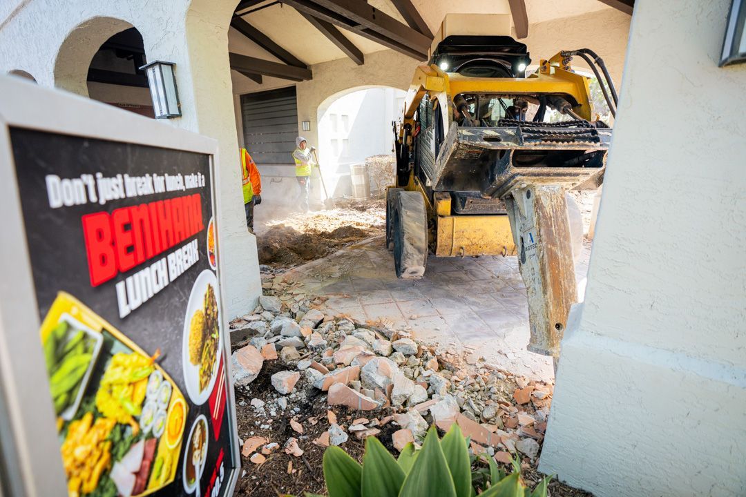 A bulldozer is demolishing a building with a sign in the foreground.