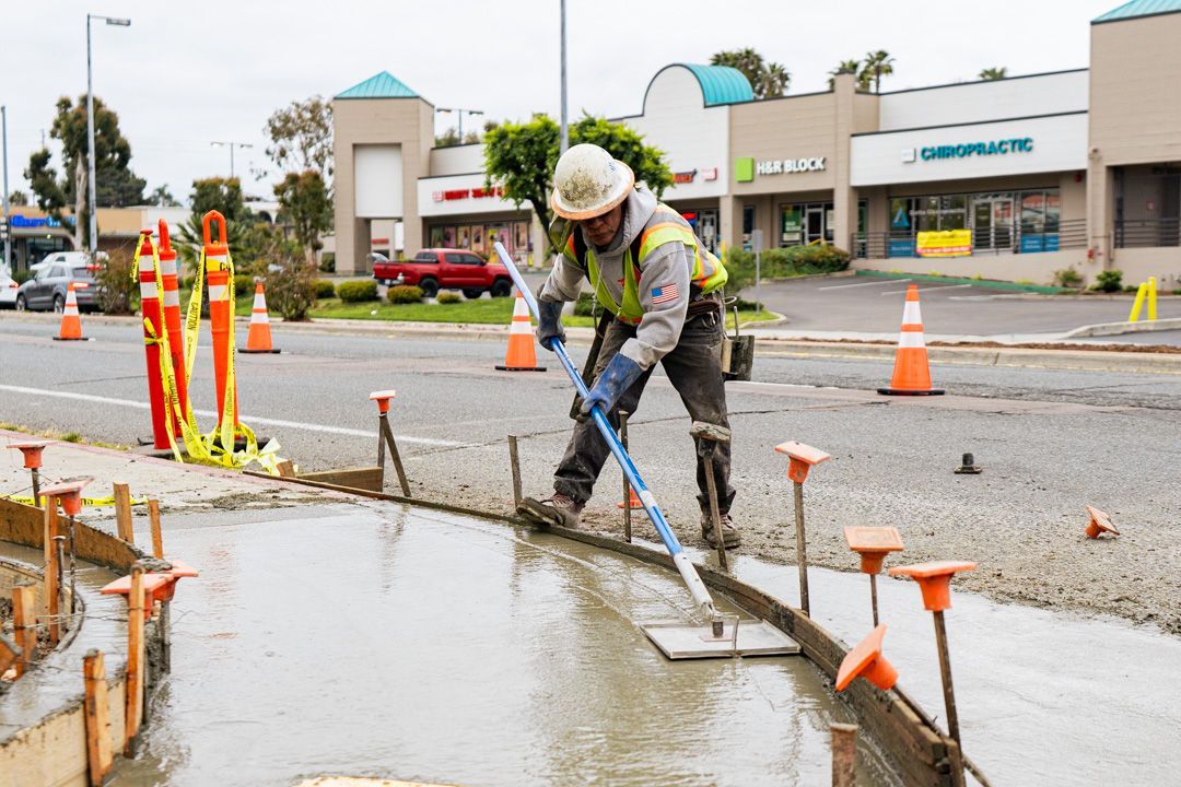 A construction worker is pouring concrete on a sidewalk.