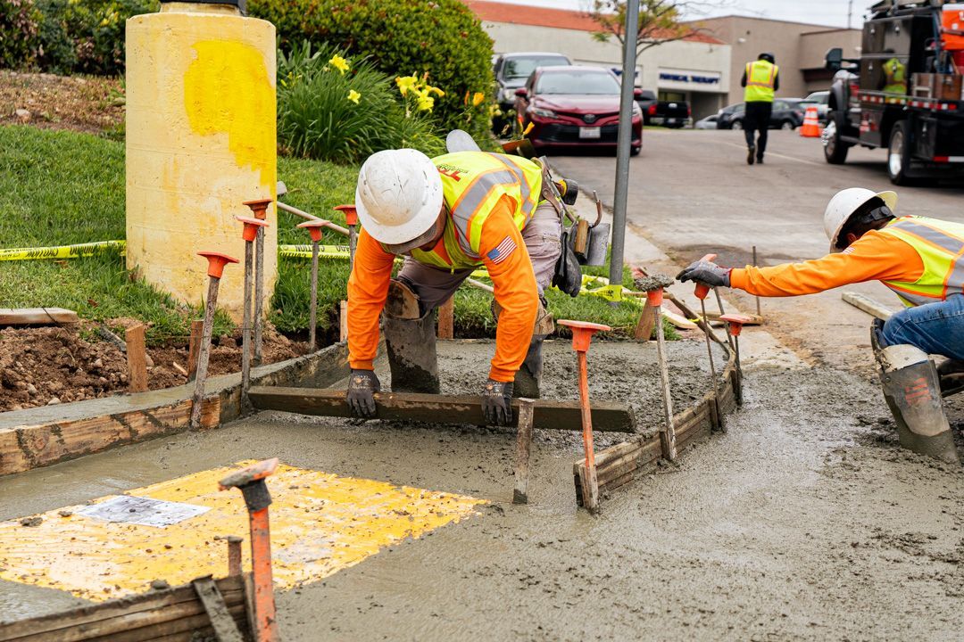 A couple of construction workers are working on a sidewalk.
