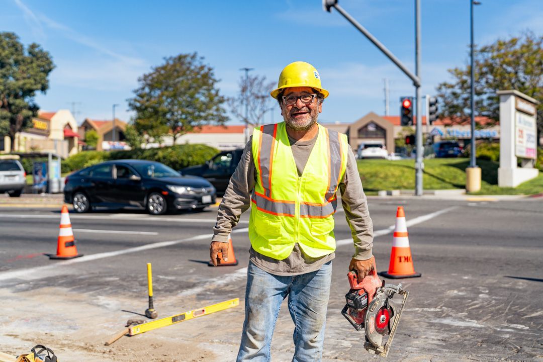 A construction worker is standing on the side of the road holding a chainsaw.
