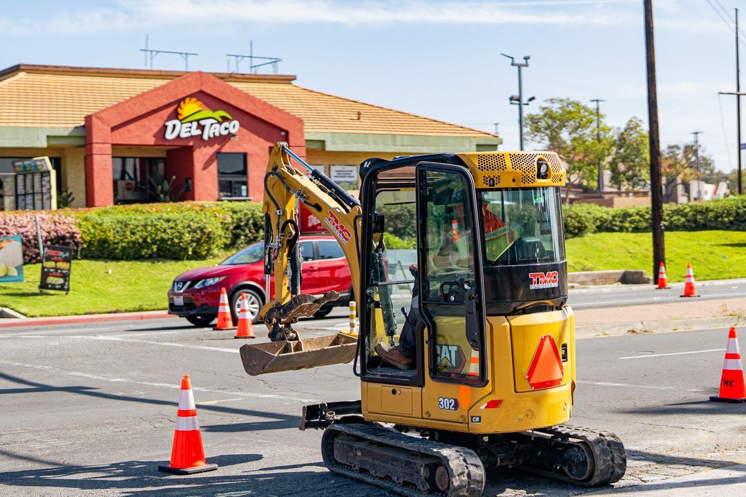 A small excavator is driving down a street in front of a restaurant.