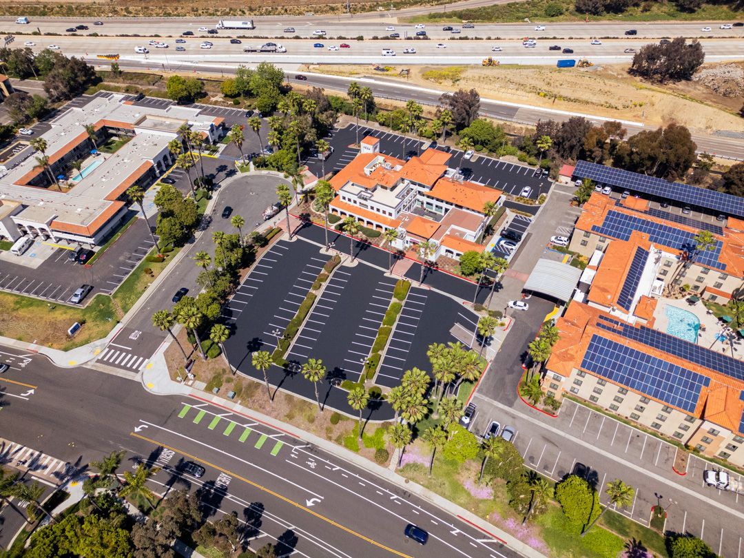 An aerial view of a hotel with a lot of parking spaces and a highway in the background.