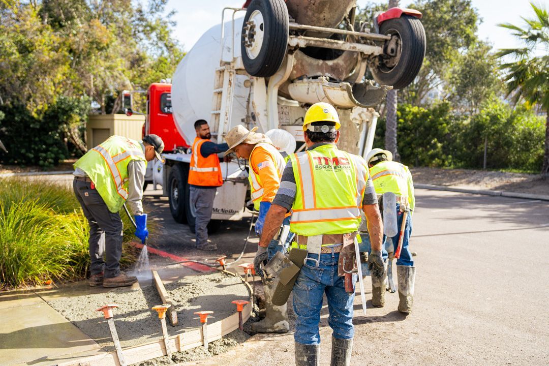 A group of construction workers are working on a sidewalk next to a concrete mixer truck.
