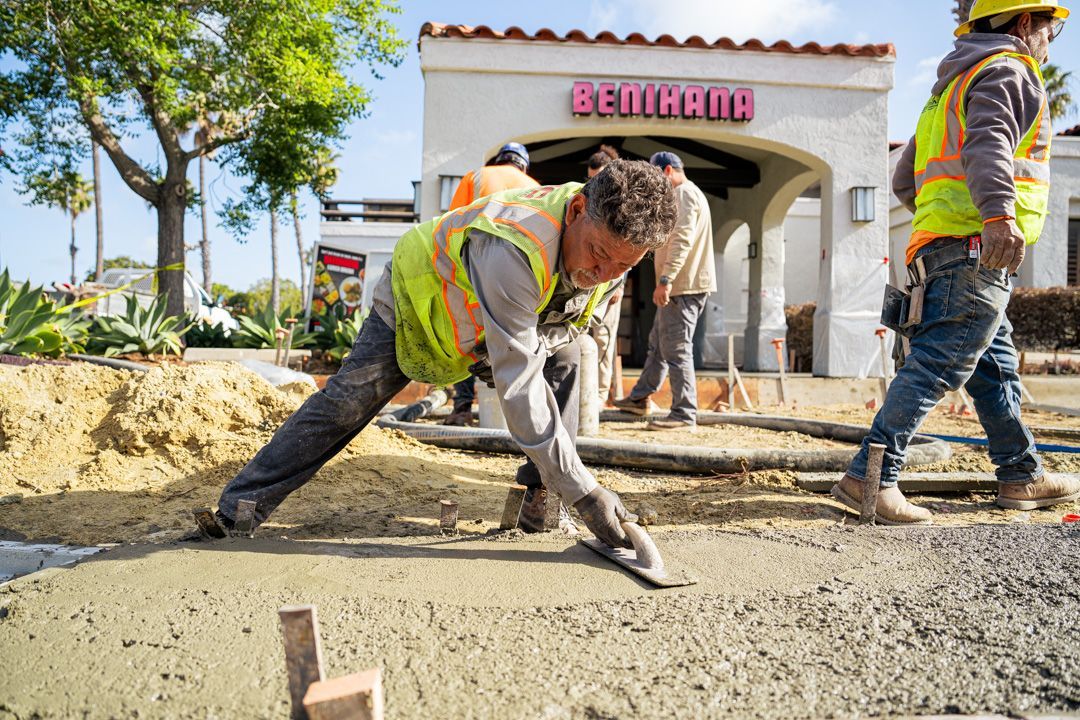 A group of construction workers are working on a sidewalk in front of a building.