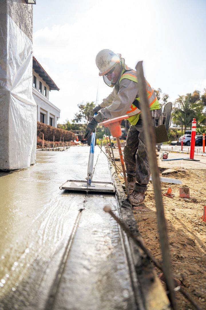A construction worker is spreading concrete on a sidewalk.