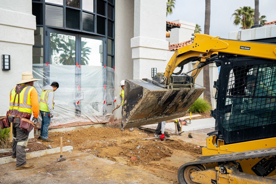 A group of construction workers are working on a sidewalk in front of a building.