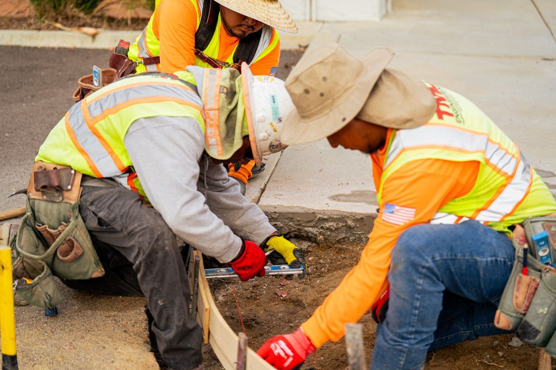 A group of construction workers are working on a sidewalk.