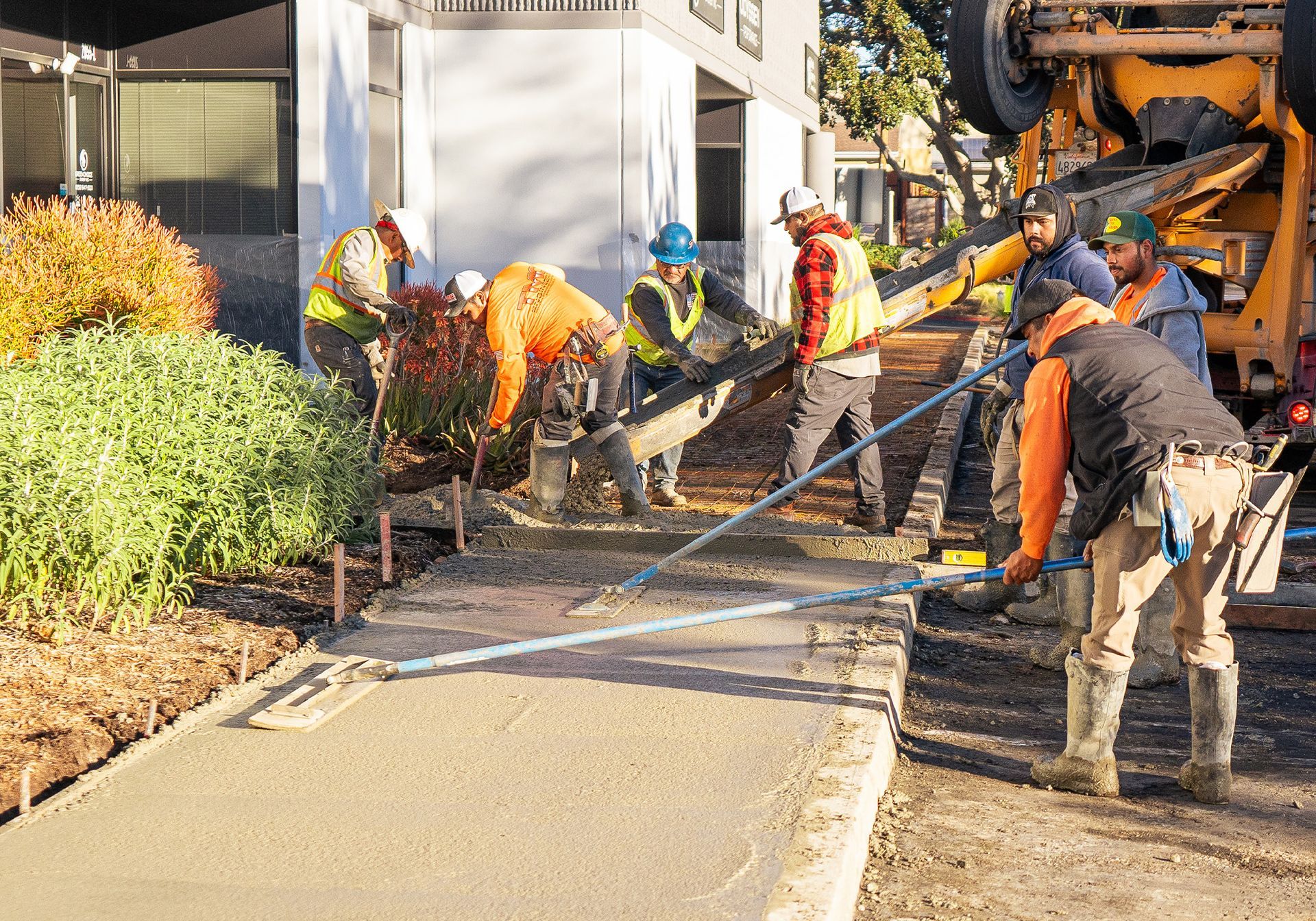 A group of construction workers are pouring concrete on a sidewalk.