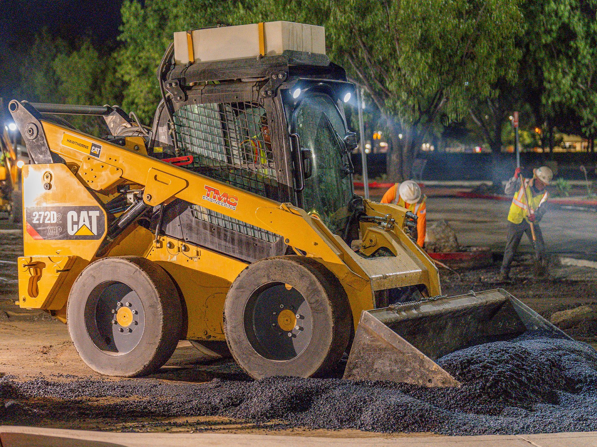 A yellow cat skid steer is working on a construction site at night.