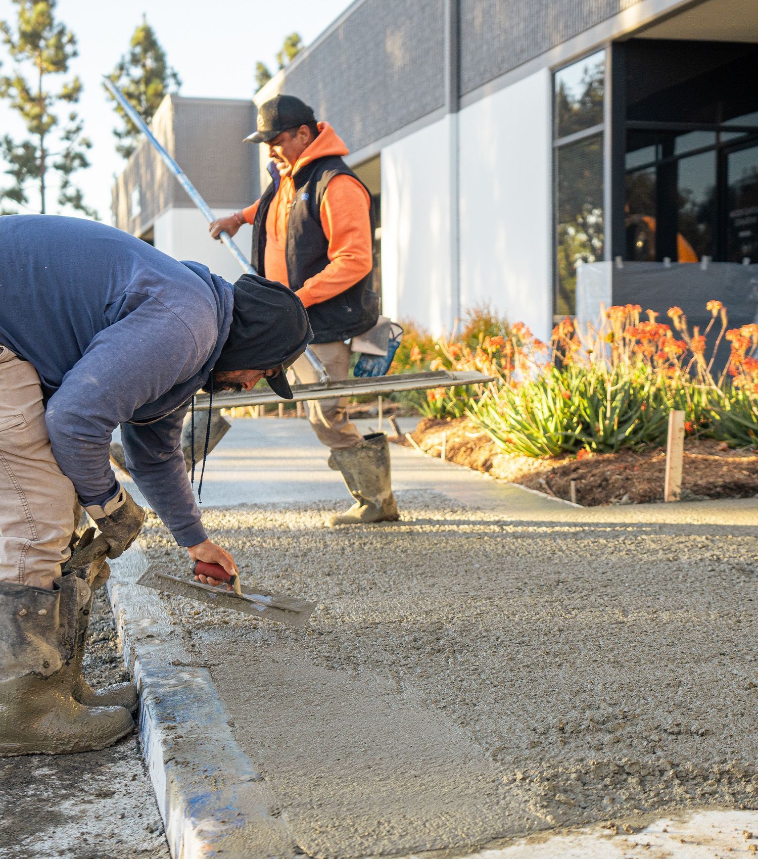 Two men are working on a sidewalk in front of a building