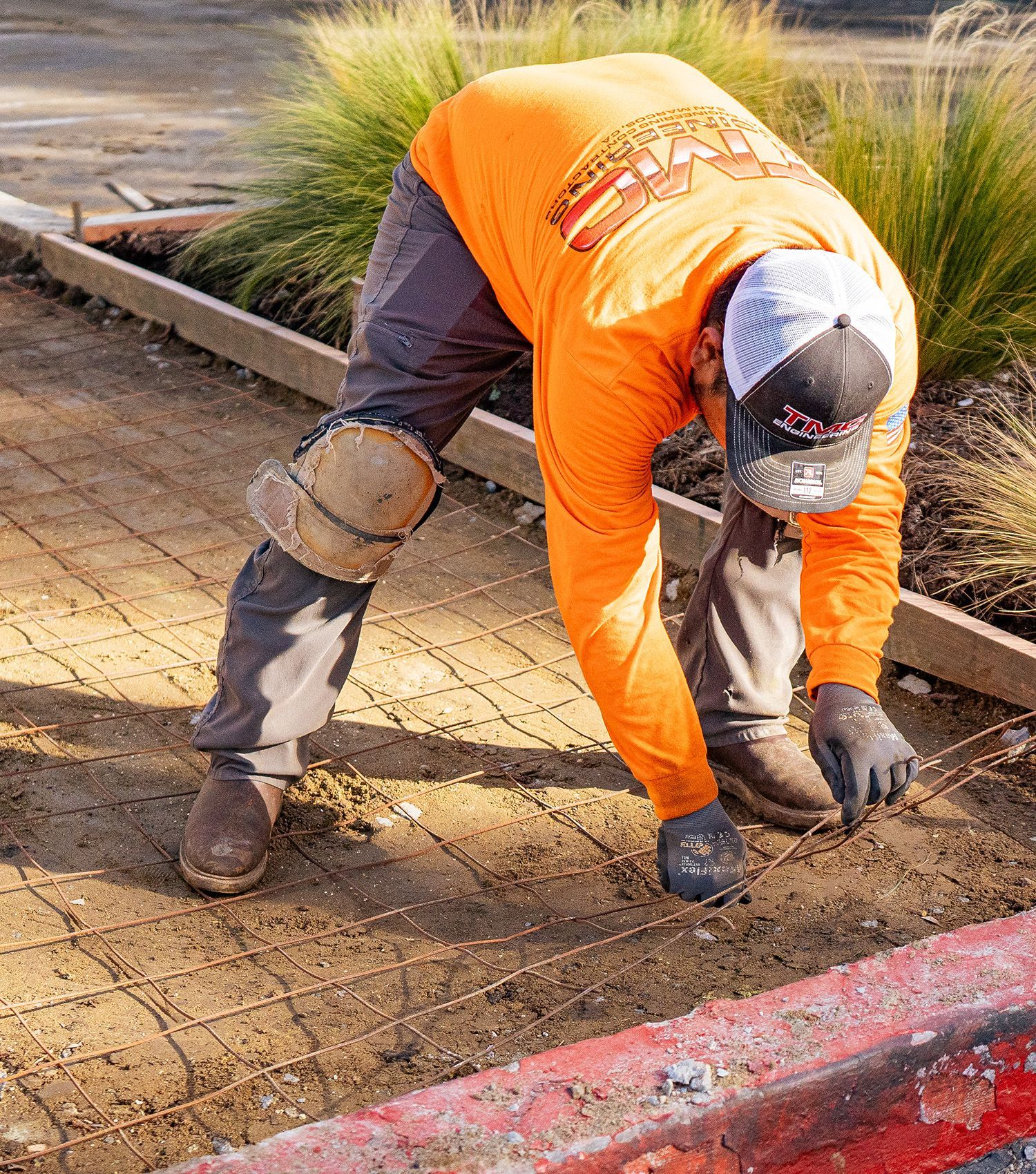 A man in an orange shirt is working on a sidewalk