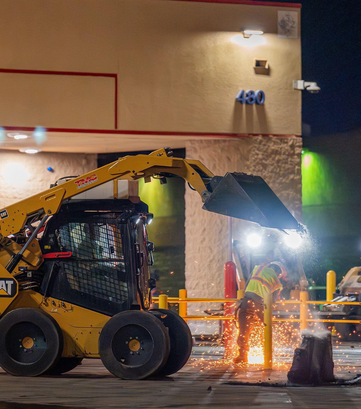 A construction worker is cutting a pole in front of a building with the number 450 on it