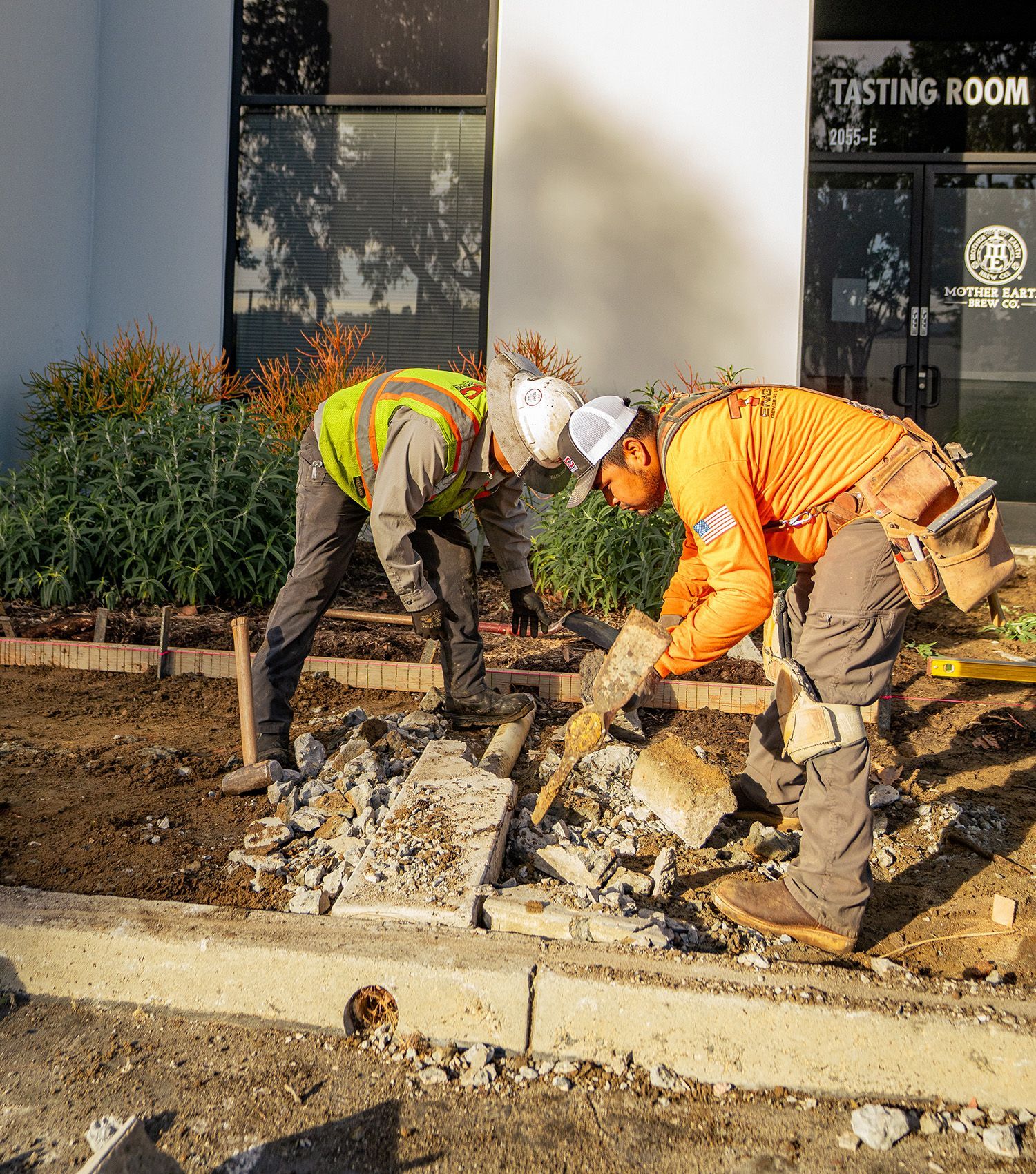 Two construction workers are working on a sidewalk in front of a building.