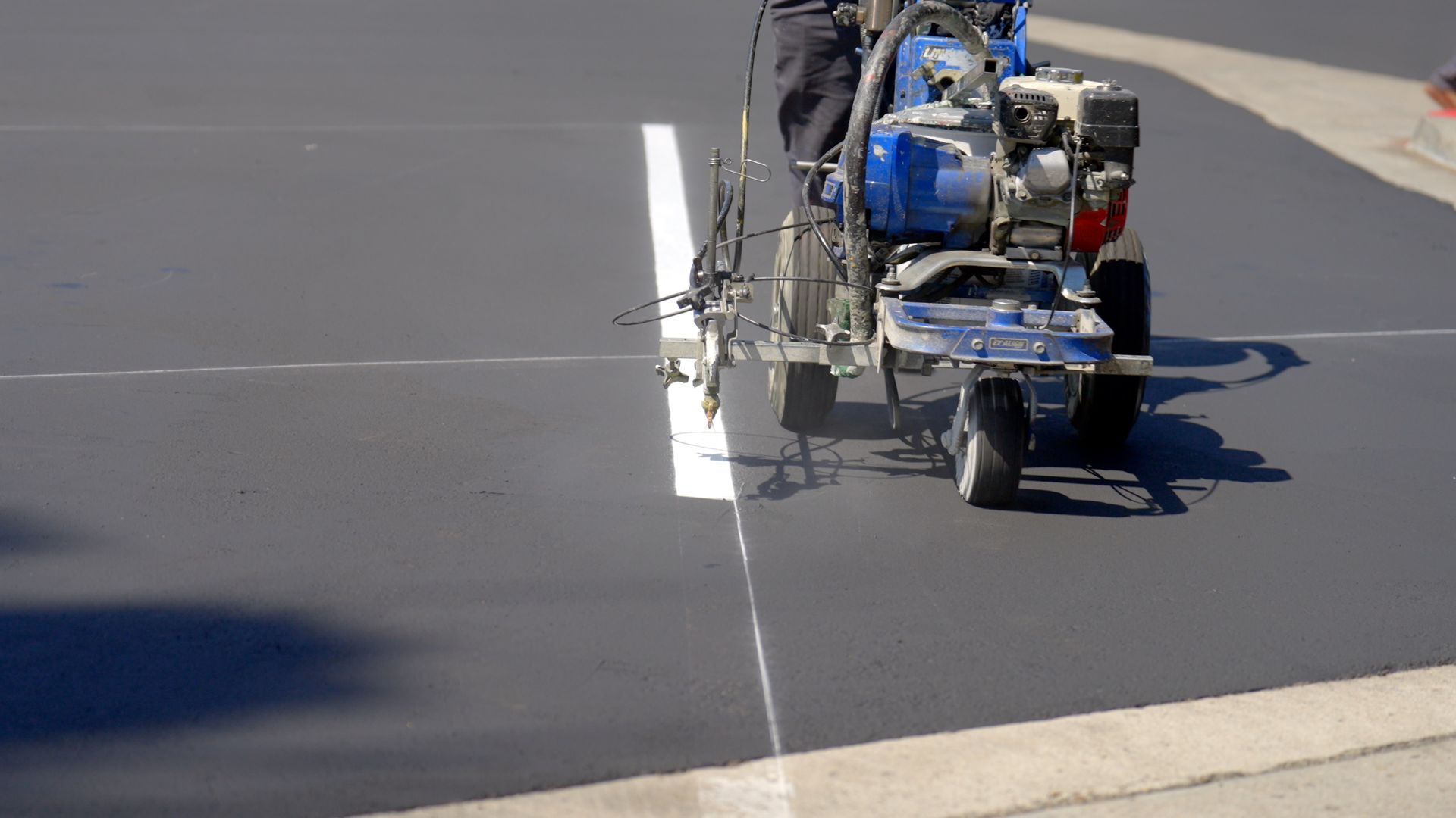A person is using a machine to paint a line on the road.