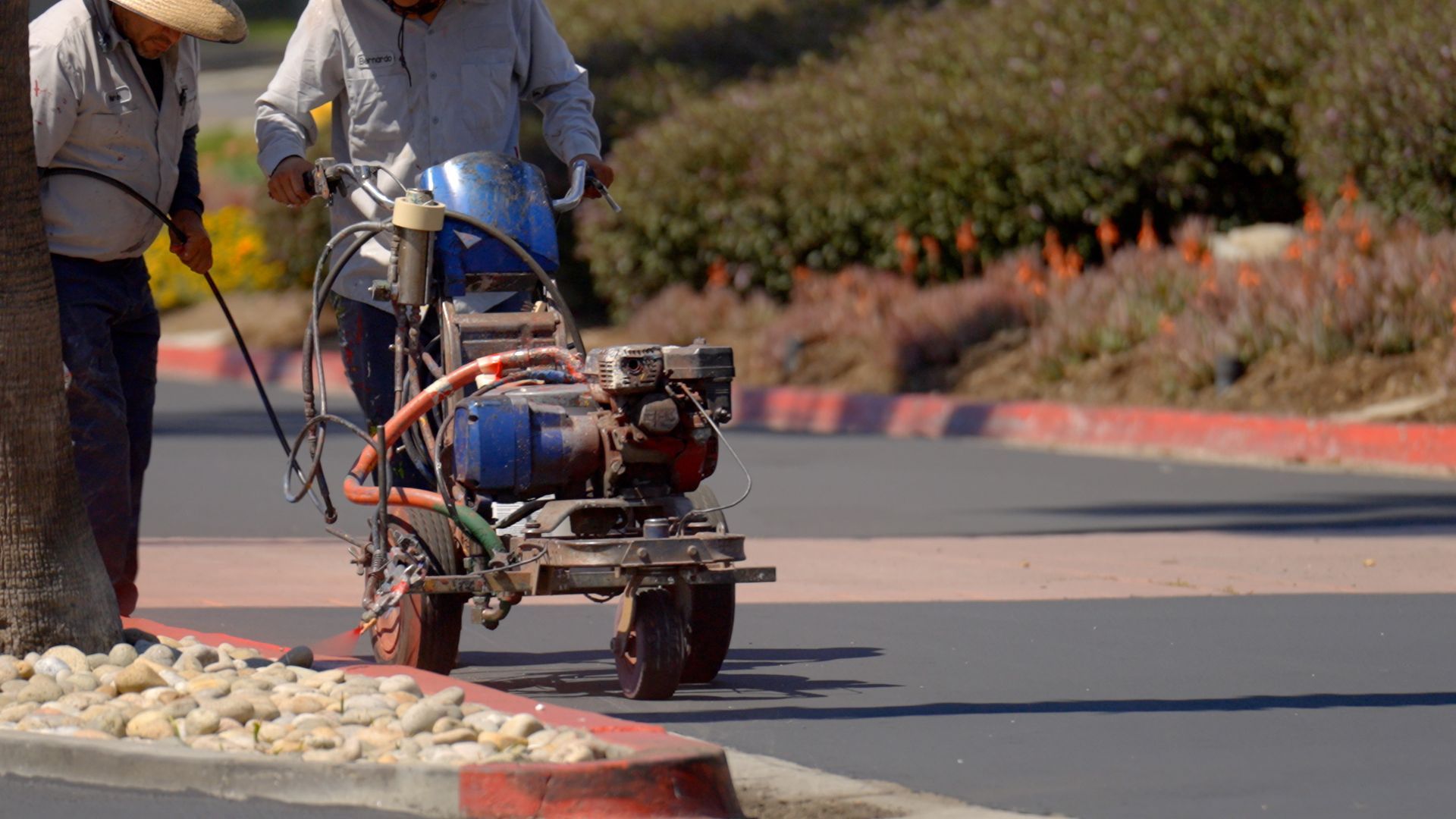 Two men are using a machine to paint a curb on a street.