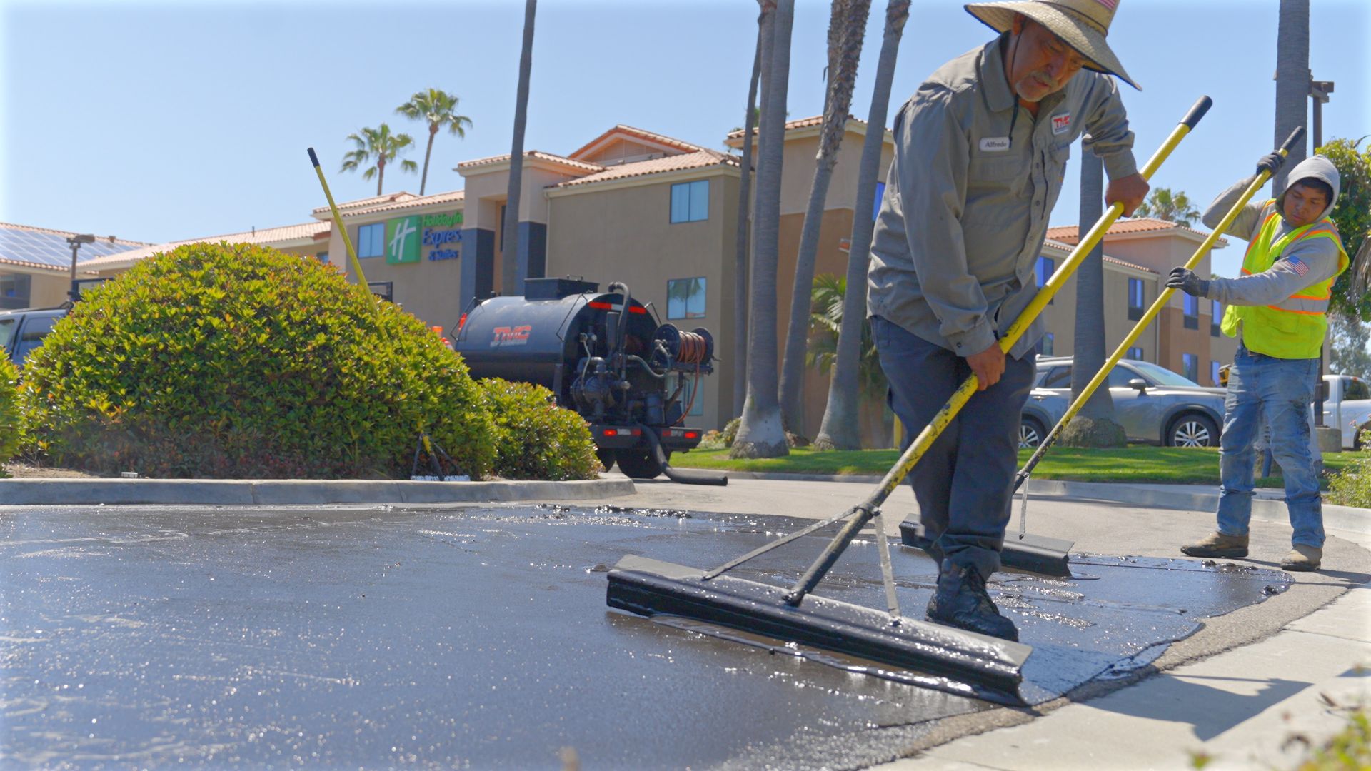 A man is using a broom to spread asphalt on a sidewalk.