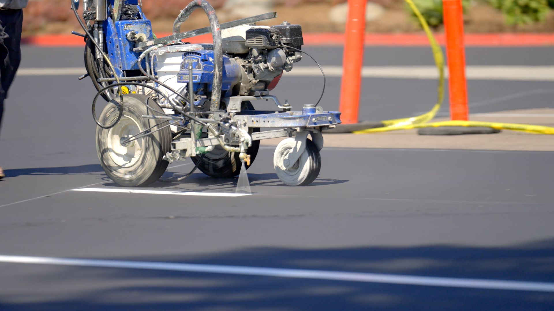 A person is walking behind a machine that is painting a line on the road.