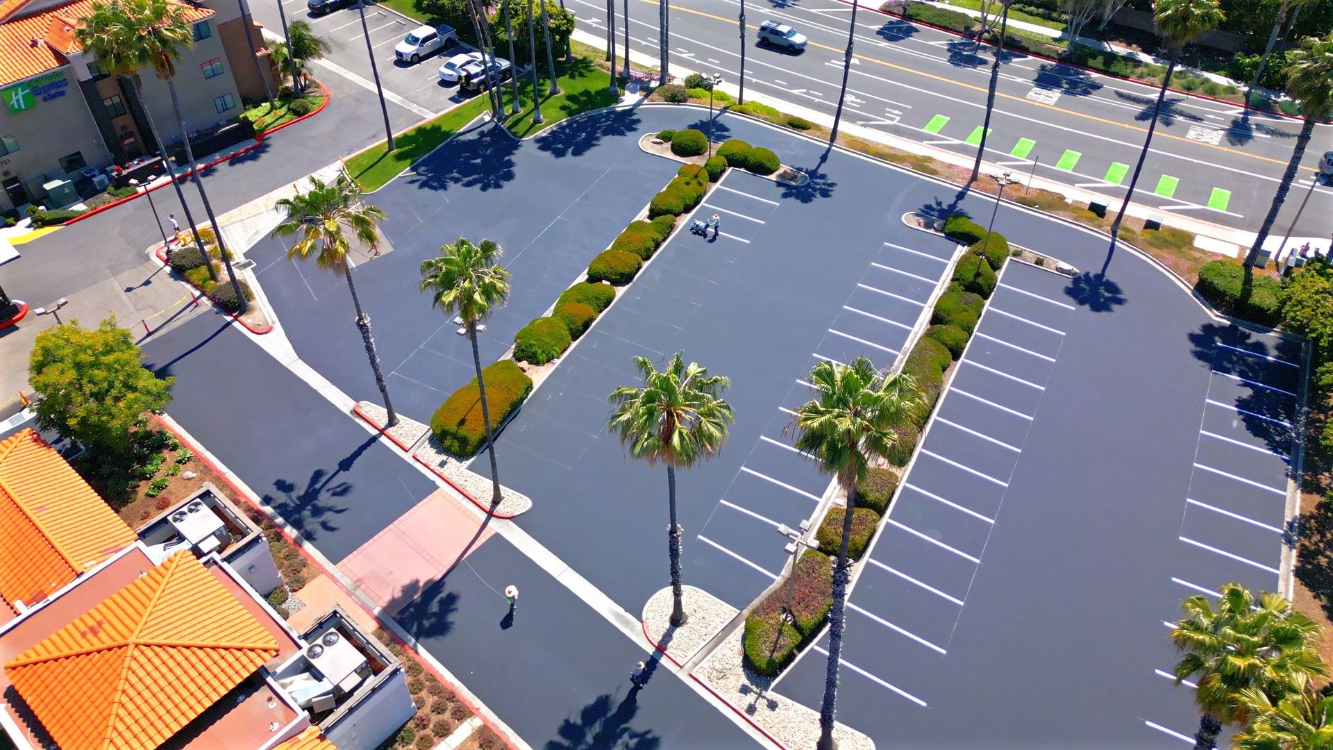 An aerial view of a parking lot with palm trees and a road.