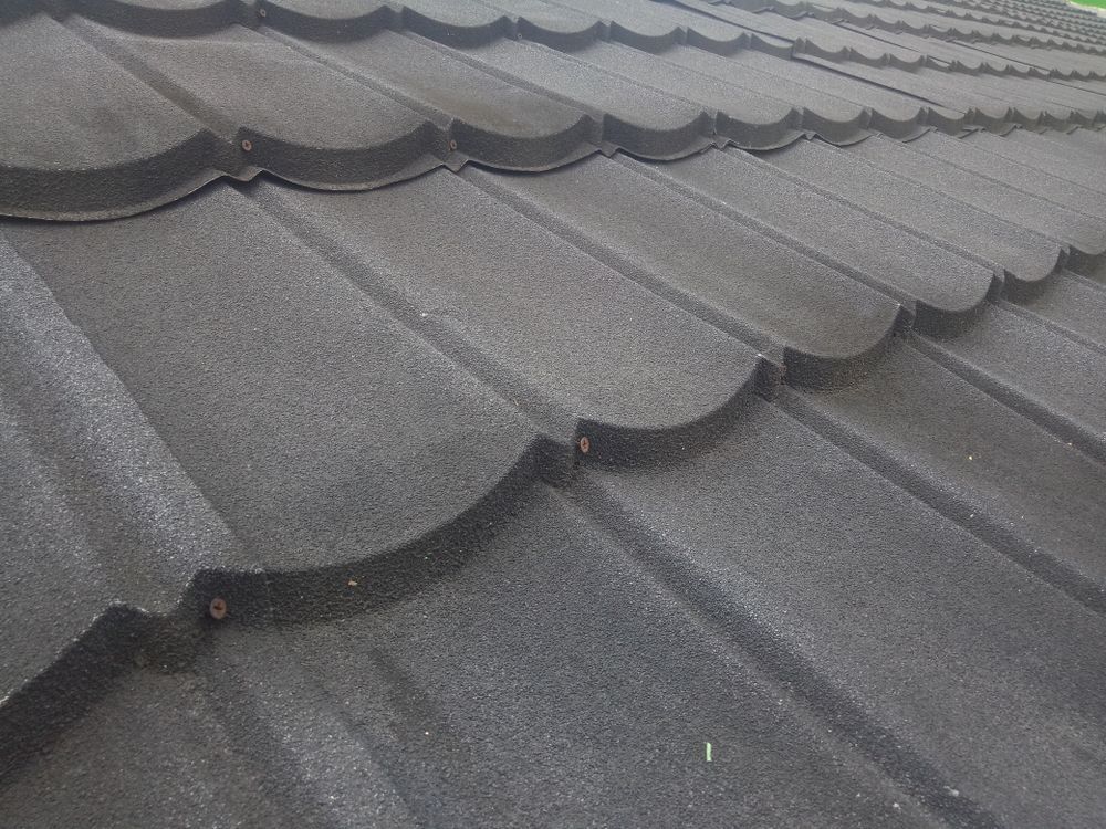 Close-up of a dark, textured metal roof with a scalloped edge, showing the overlapping tiles.