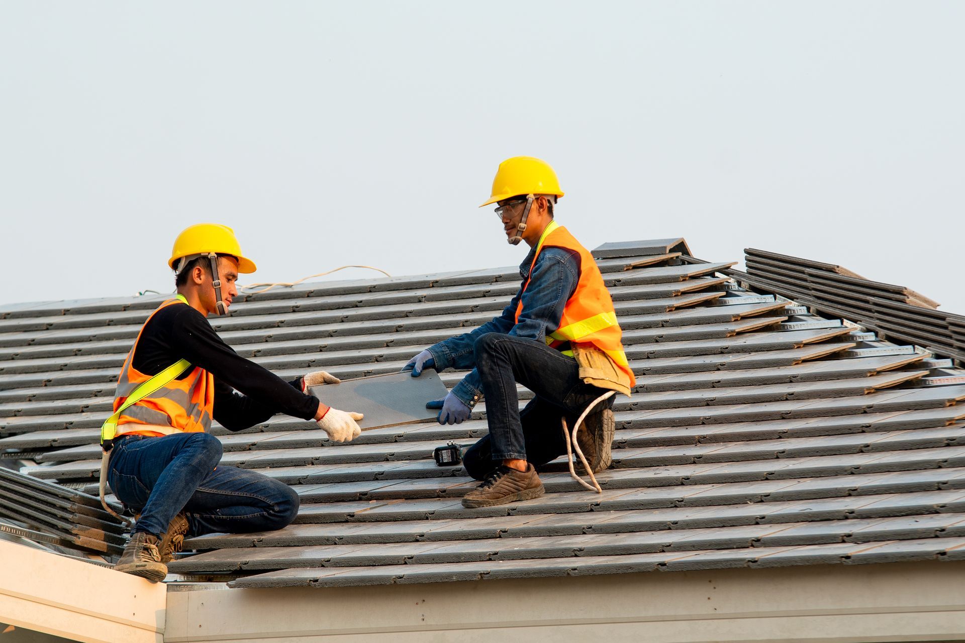 Two construction workers are working on the roof of a house.