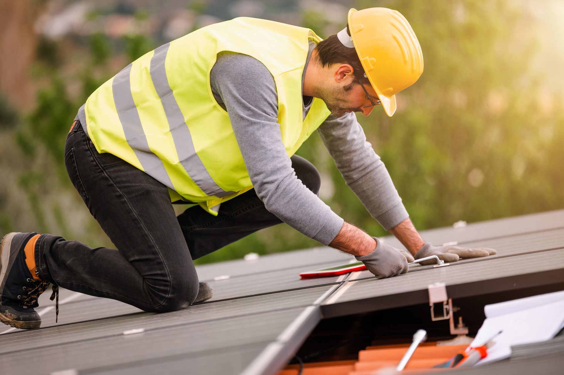 A man wearing a hard hat and safety vest is working on a roof.