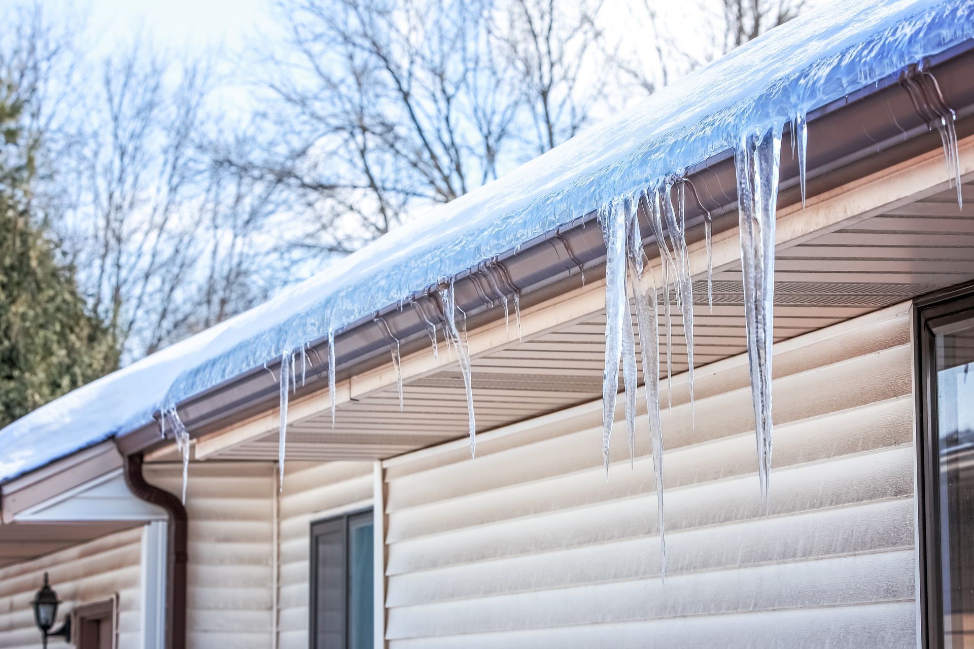 Icicles hanging from a house roof in winter; light beige siding.