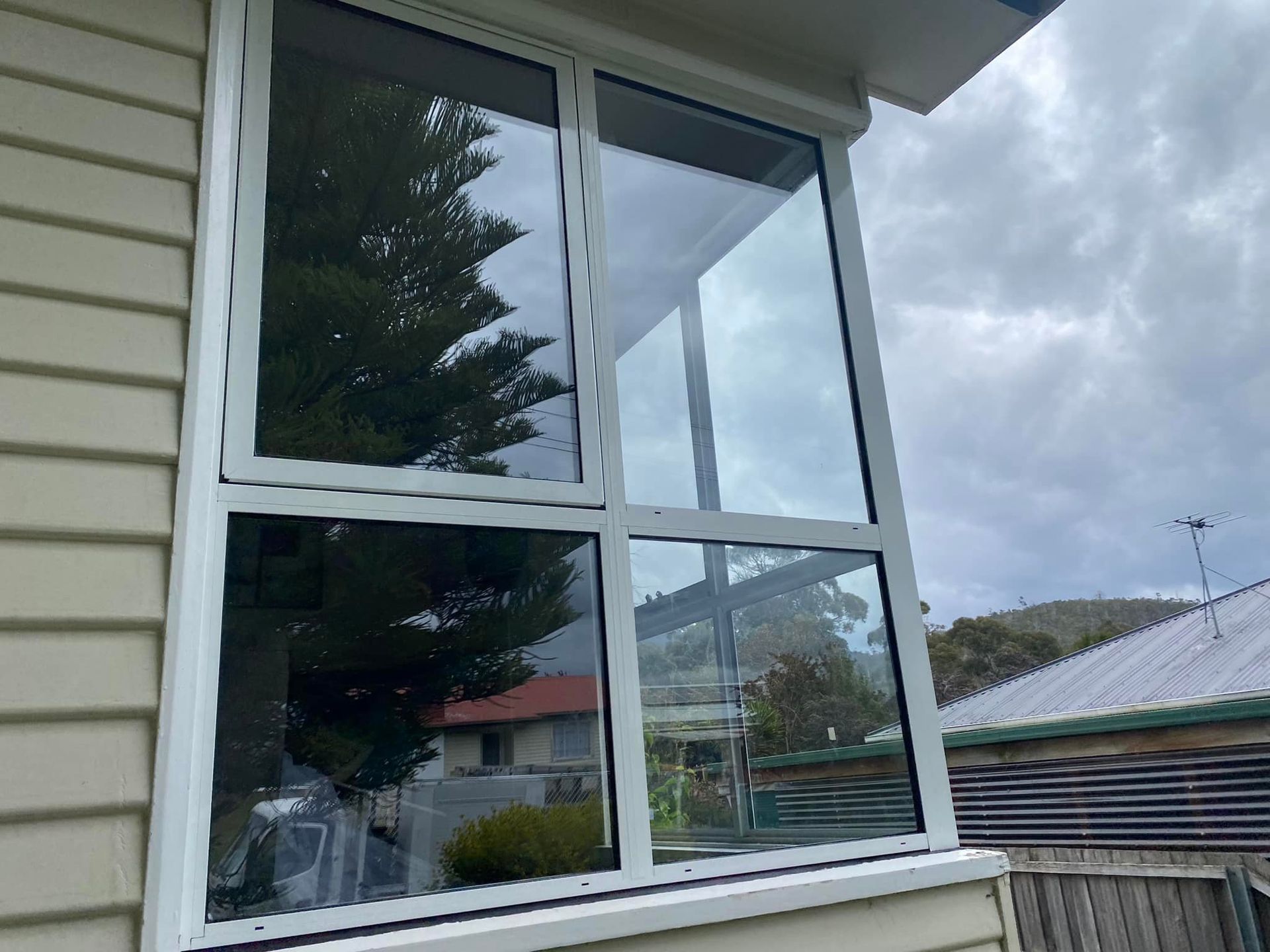 A large window on the side of a house with trees reflected in it.