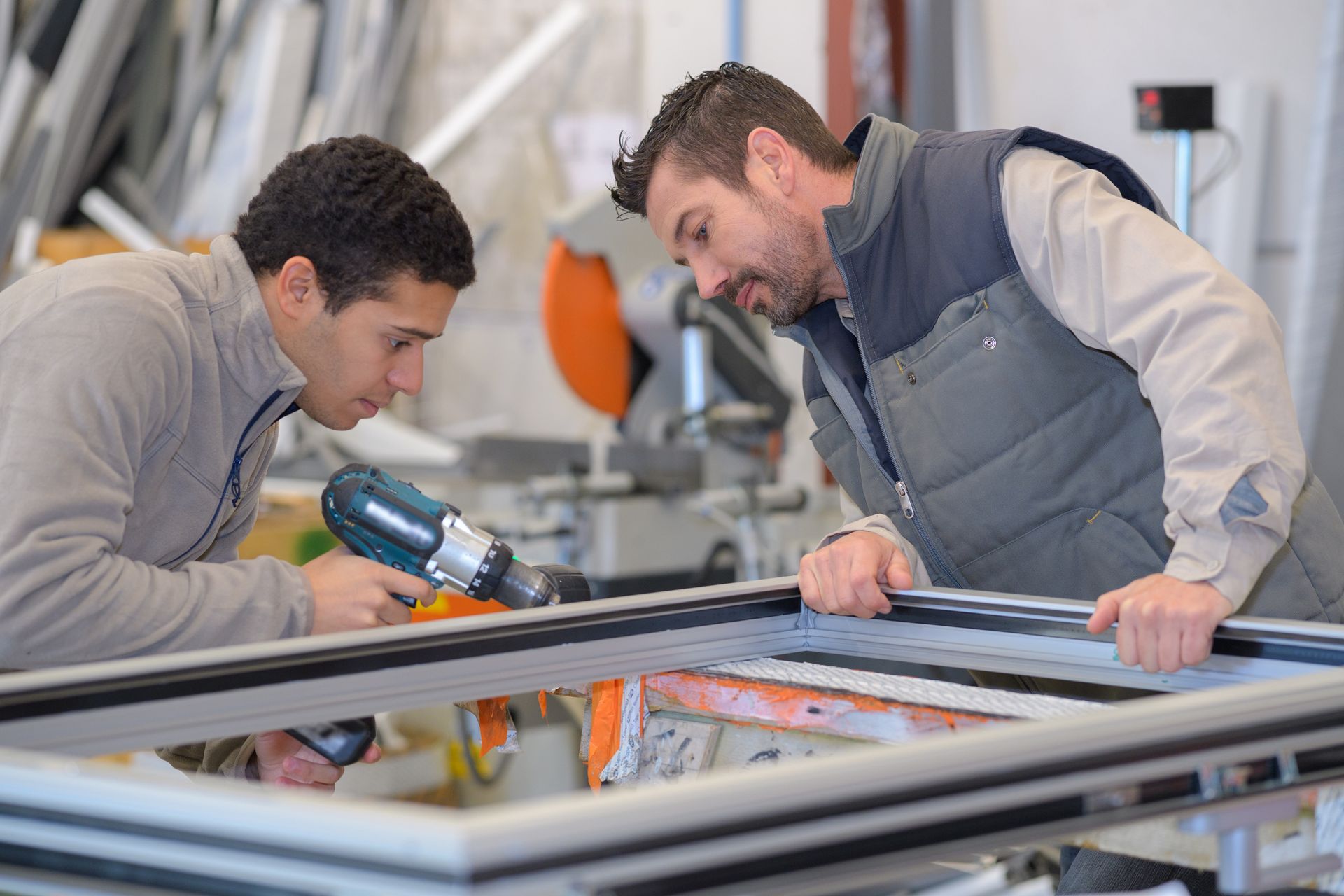 Two male workers assembling an aluminium window frame in a glass factory workshop. Two male workers assembling an aluminium window frame in a glass factory workshop.