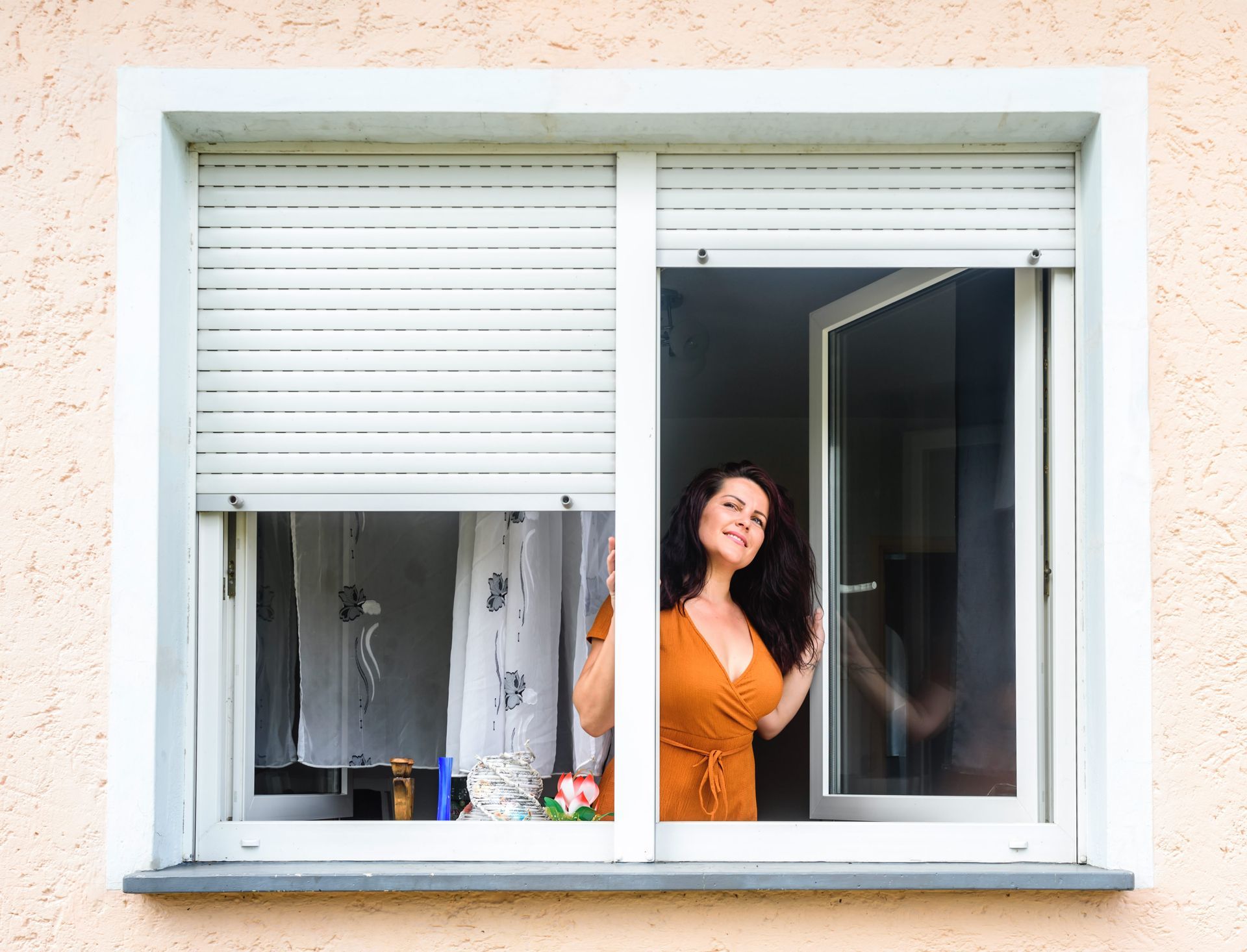 An outside view of a young woman opens a double-glazed window with blinds