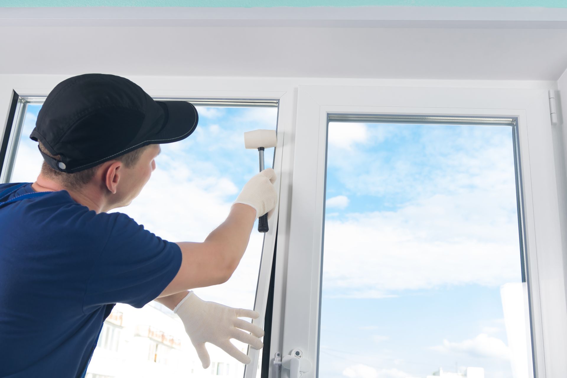 A builder installs a double-glazed window, hammering it with a rubber mallet.