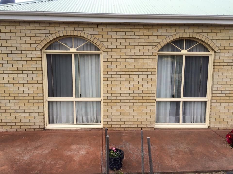 A brick building with two arched windows and white curtains