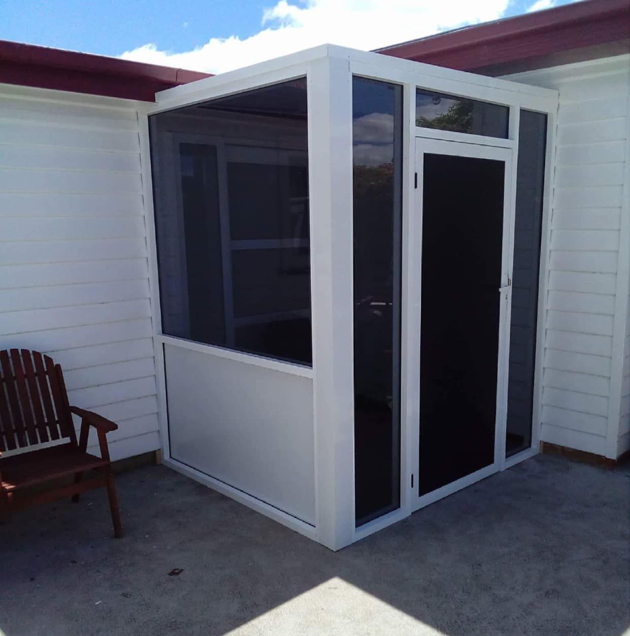 A white building with a screened in porch and a bench