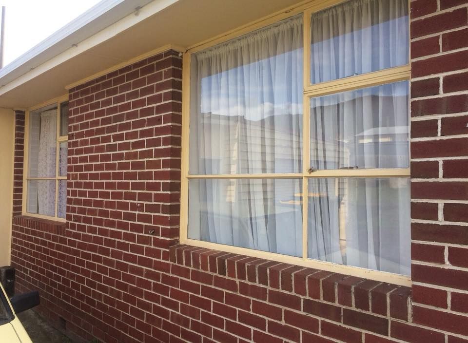 A brick building with two windows and white curtains