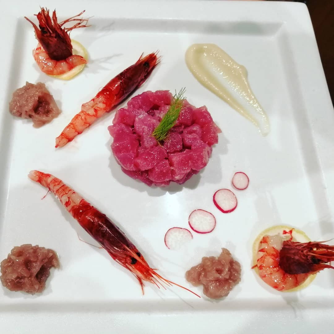 Un piatto bianco con sopra gamberi e un fiore rosa