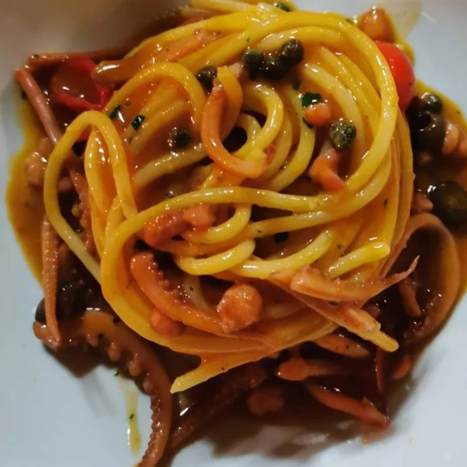 Un primo piano di un piatto di spaghetti con polpo e pomodori