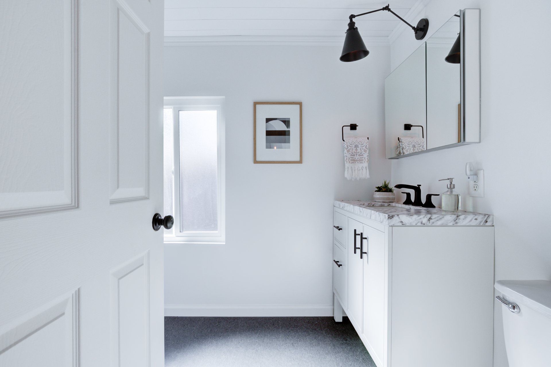 A bathroom with white cabinets , a sink , a mirror and a window.