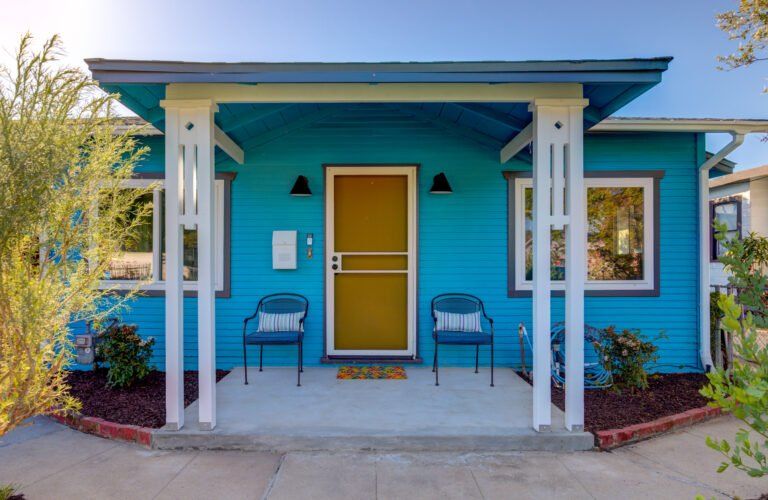 A blue house with a yellow door and chairs on the porch.