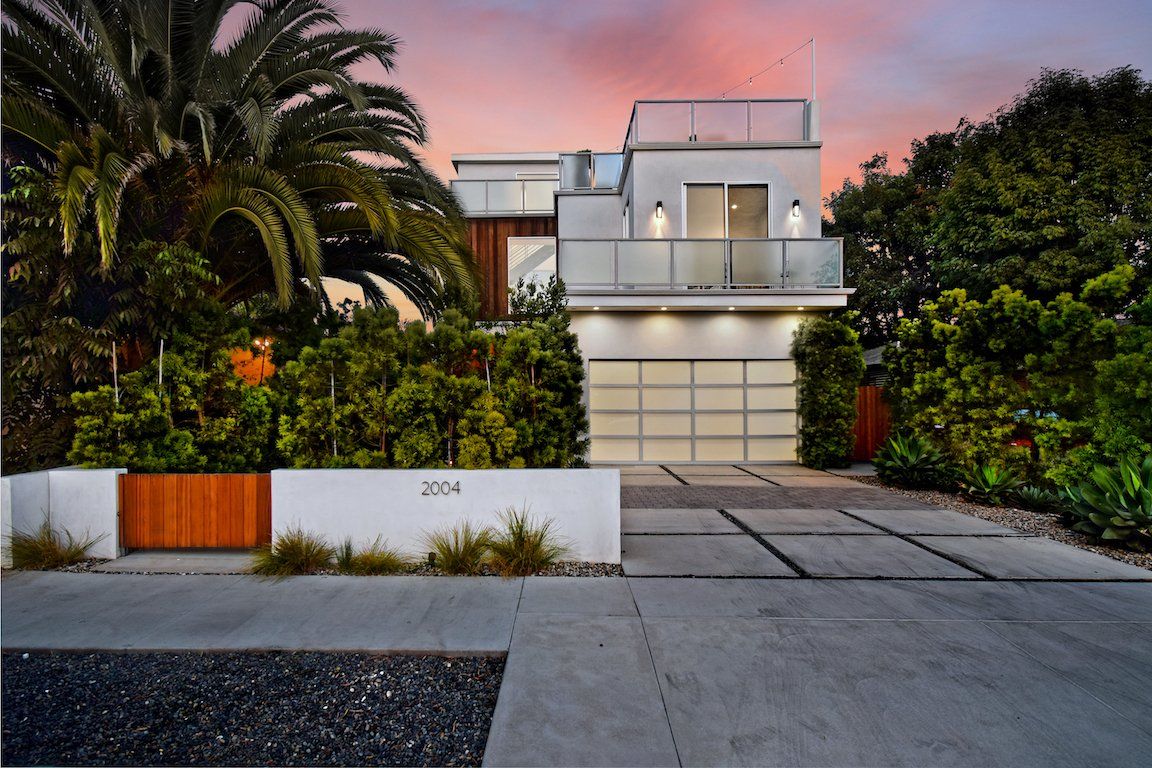 A modern house with a concrete driveway and a palm tree in front of it.
