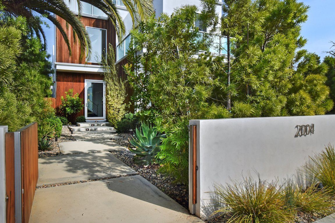 The front of a house with a walkway leading to it surrounded by trees and bushes.
