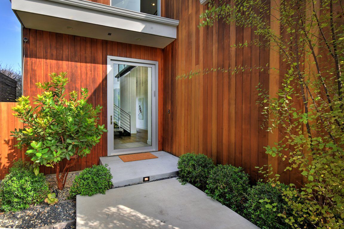 The front door of a house with wooden siding and a concrete walkway leading to it.
