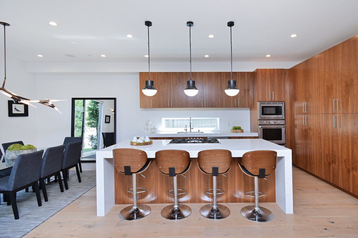 A kitchen with a large island and stools and a dining room in the background.