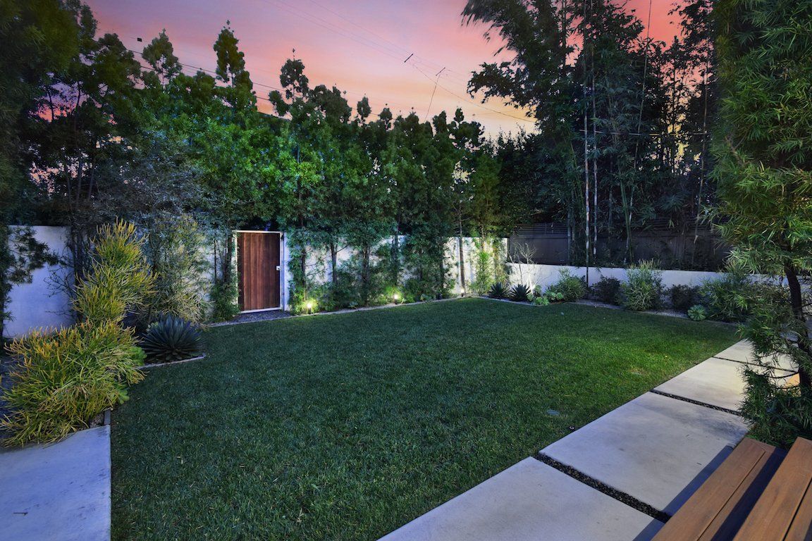 A backyard with a lush green lawn and trees at sunset