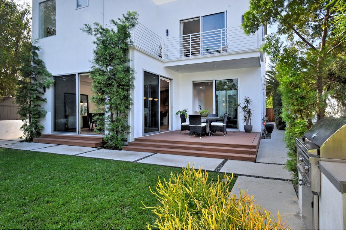 A large white house with a patio and a grill in the backyard.