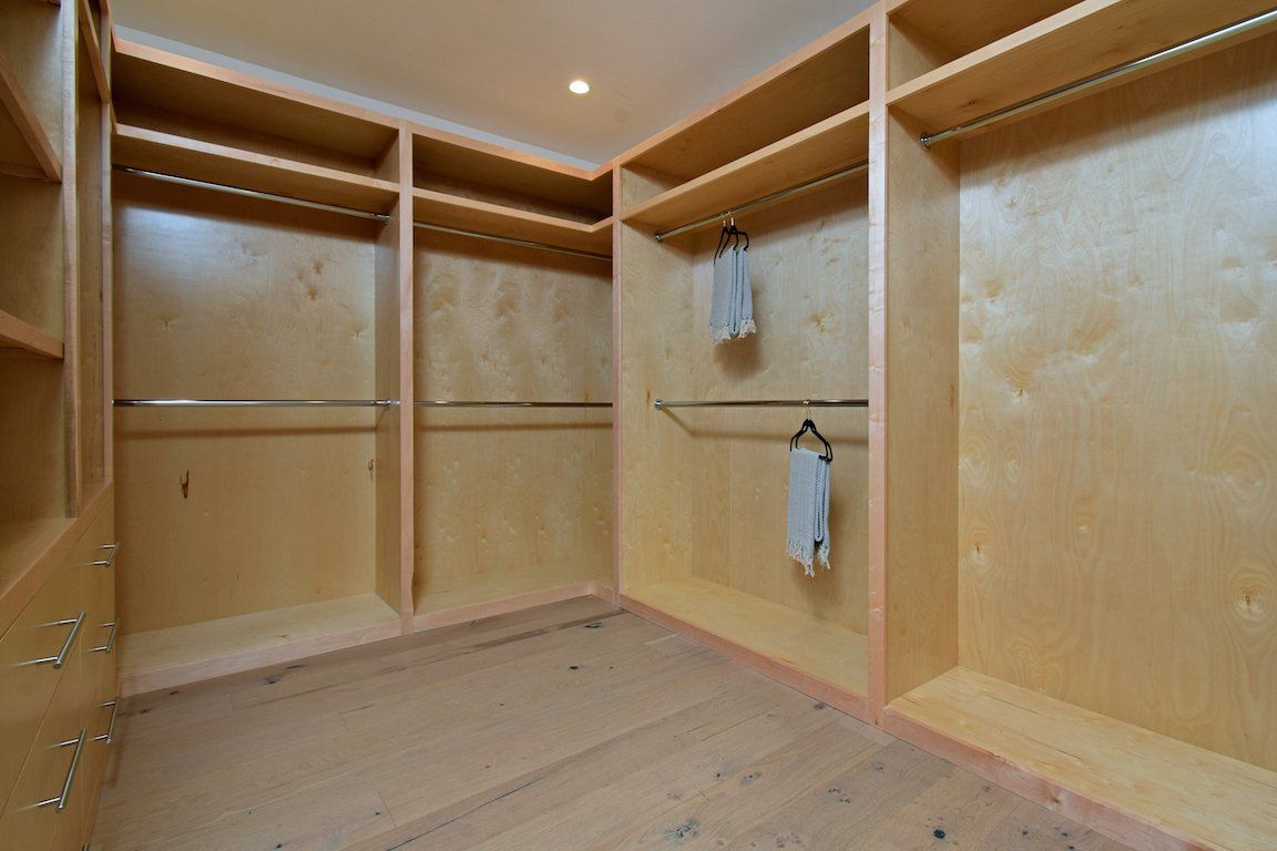 An empty walk in closet with wooden shelves and clothes hanging on racks.