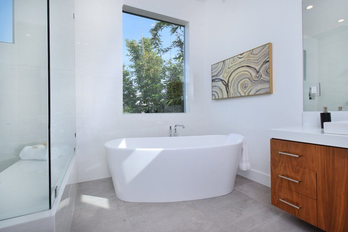 A bathroom with a tub , sink , mirror and window.